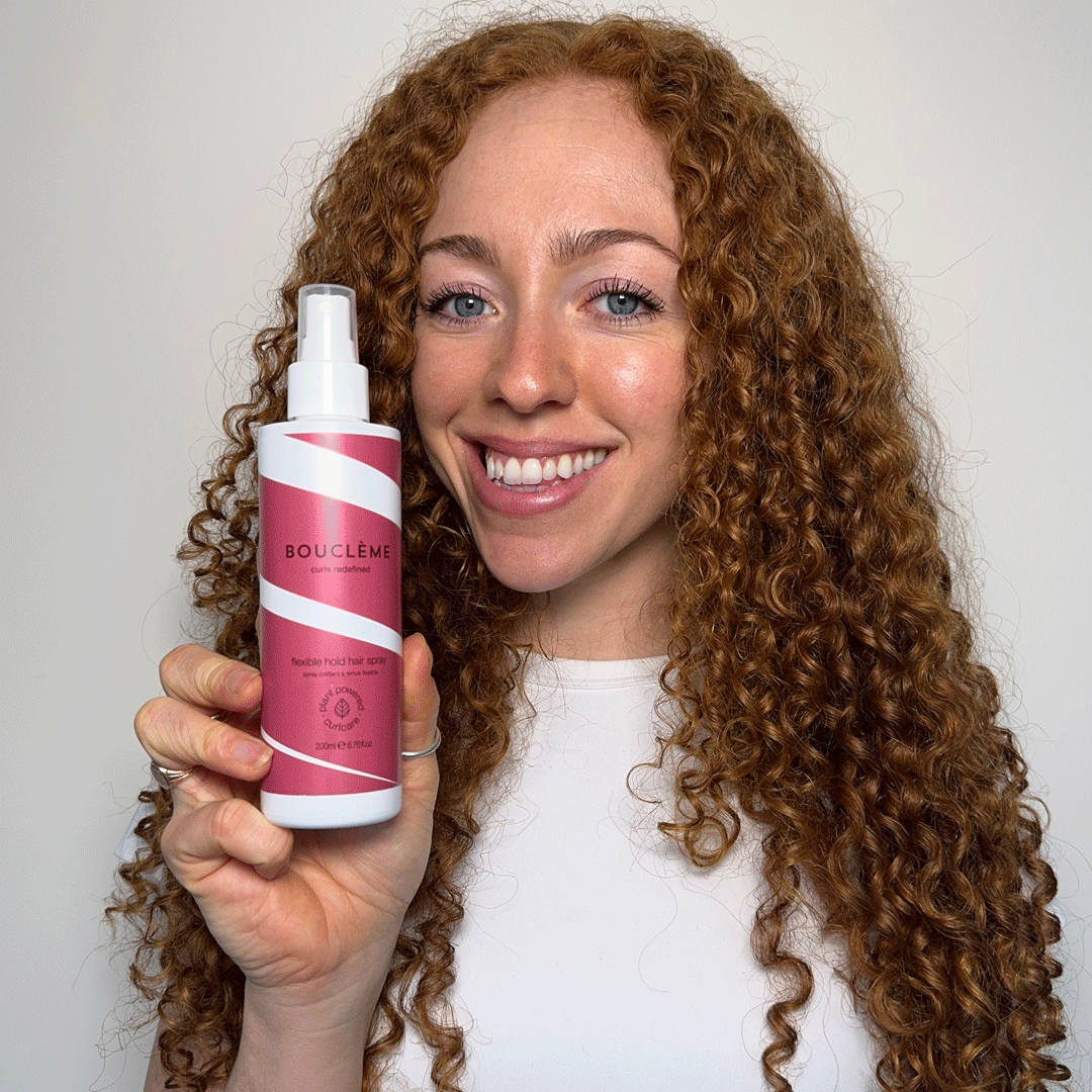 Model applying flexible hold hair spray on dry curly hair to fix the style in place