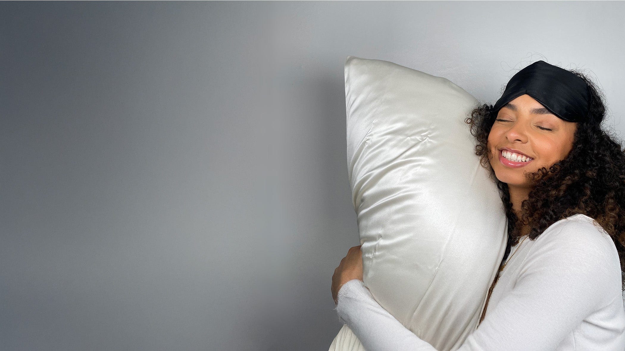 A woman with curly hair rests on a silk pillowcase, her curls still looking fresh in the morning light.