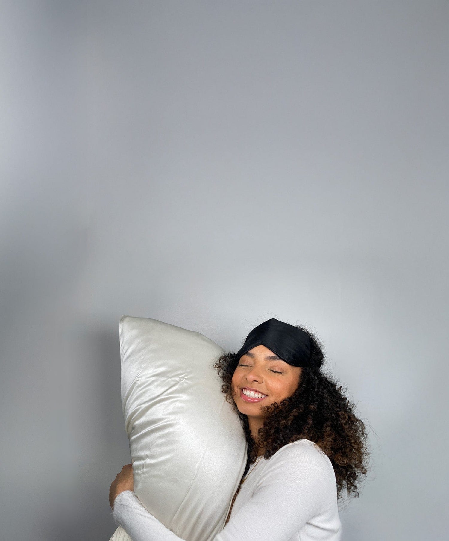 A woman with curly hair rests on a silk pillowcase, her curls still looking fresh in the morning light.